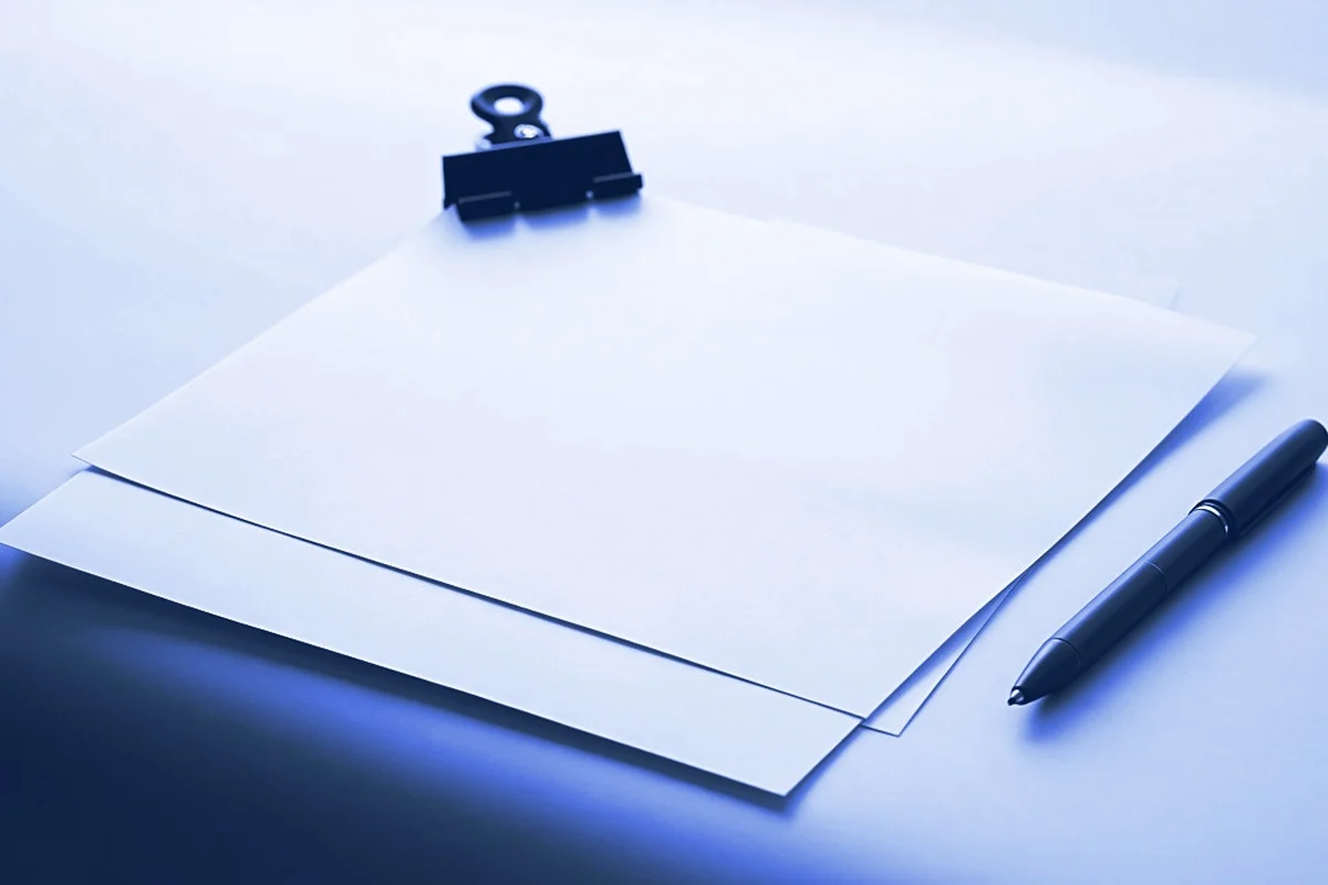 Two plain printed pages held by a black bulldog clip beside a red pen, for the AI trainer resume template guide